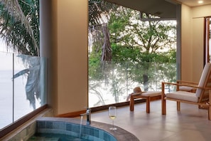 A modern indoor pool area with a glass balustrade, a lounge chair, and a glass of wine. - Arenas del Mar Beachfront & Rainforest Resort (Quepos)