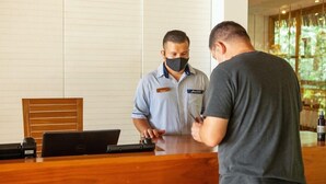 A reception desk with a laptop, a wooden chair, and a name tag on the staff member. - Arenas del Mar Beachfront & Rainforest Resort (Quepos)