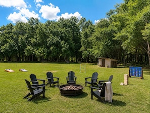 A grassy outdoor area with several Adirondack chairs, a fire pit, and a small shed. - 5-Acre Soaring Hawk Retreat | 6Br sleeps 12 | Tampa (Seffner)