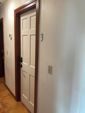A hallway with a white door, a number '3' sign, a light switch, and a thermostat. - 6BR Home for Families & Groups (Seffner)