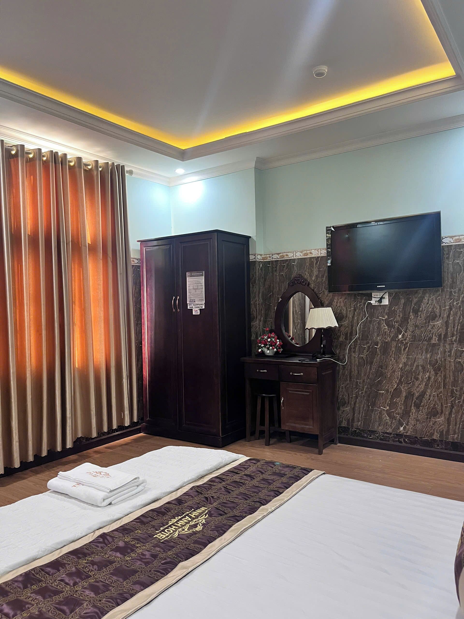 A hotel room with a bed, a desk with a mirror, a wardrobe, and a television on the wall.