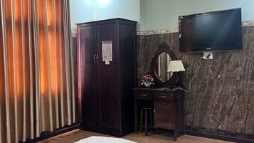 A hotel room with a bed, a desk with a mirror, a wardrobe, and a television on the wall.