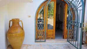 A rustic entrance with a wooden door and metal gate, a large vase, and a stone-paved path leading inside. - Charming home with private entrance in historic villa – quiet & idyllic (Ostuni)