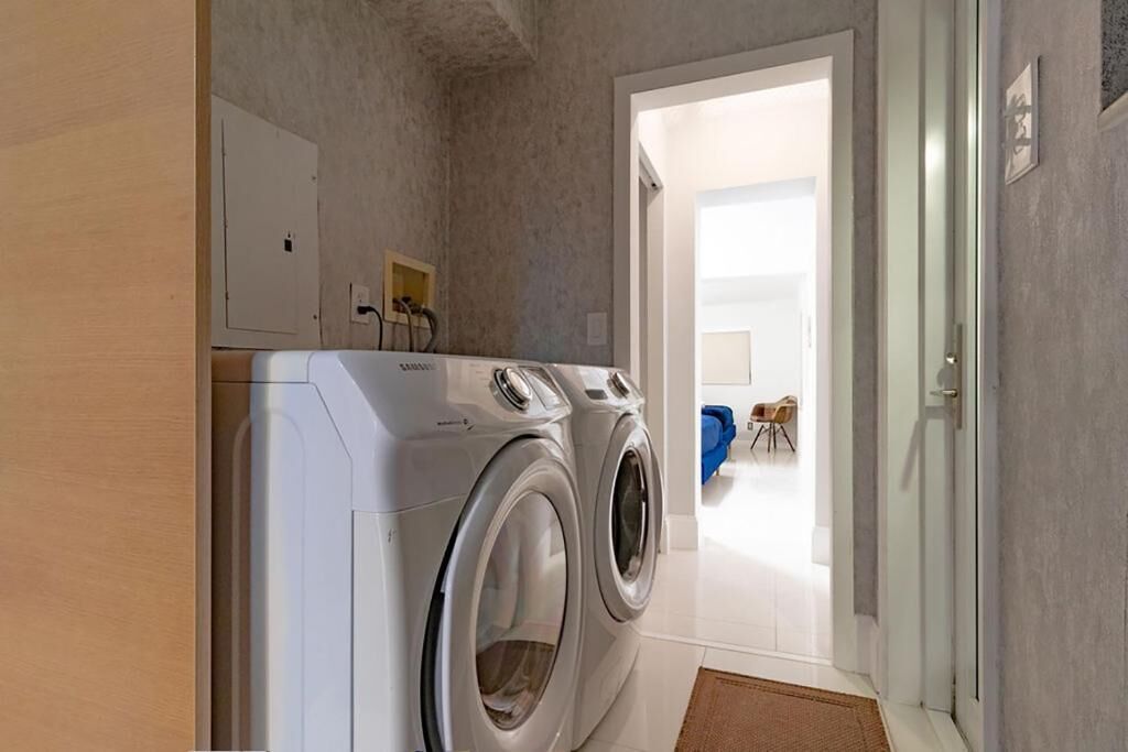 A laundry area with two front-loading washing machines, a white door leading to a room with a blue chair, and a small wooden cabinet.
