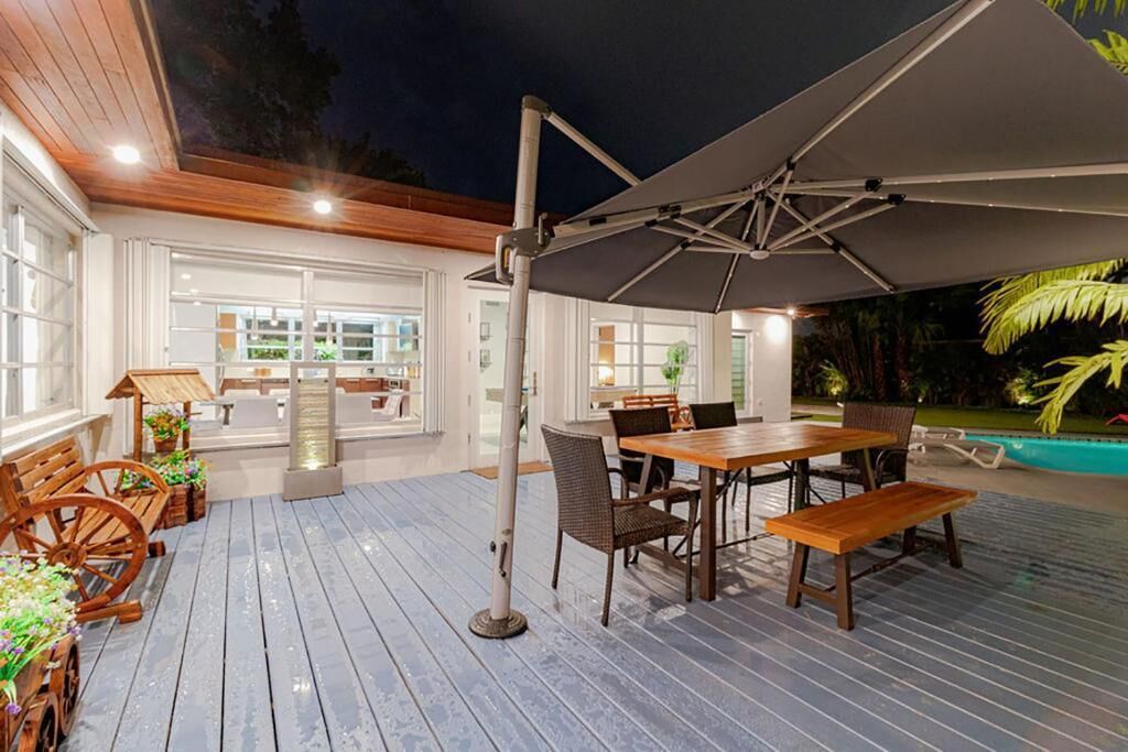 Une terrasse extérieure avec une table et des chaises en bois, un grand parasol et une piscine en arrière-plan.