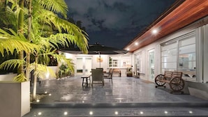 A covered outdoor area with a wooden bench, a wheelchair, and a table under a canopy. - Villa Oahu Basketball Fire Pit Mini Golf (North Miami Beach)