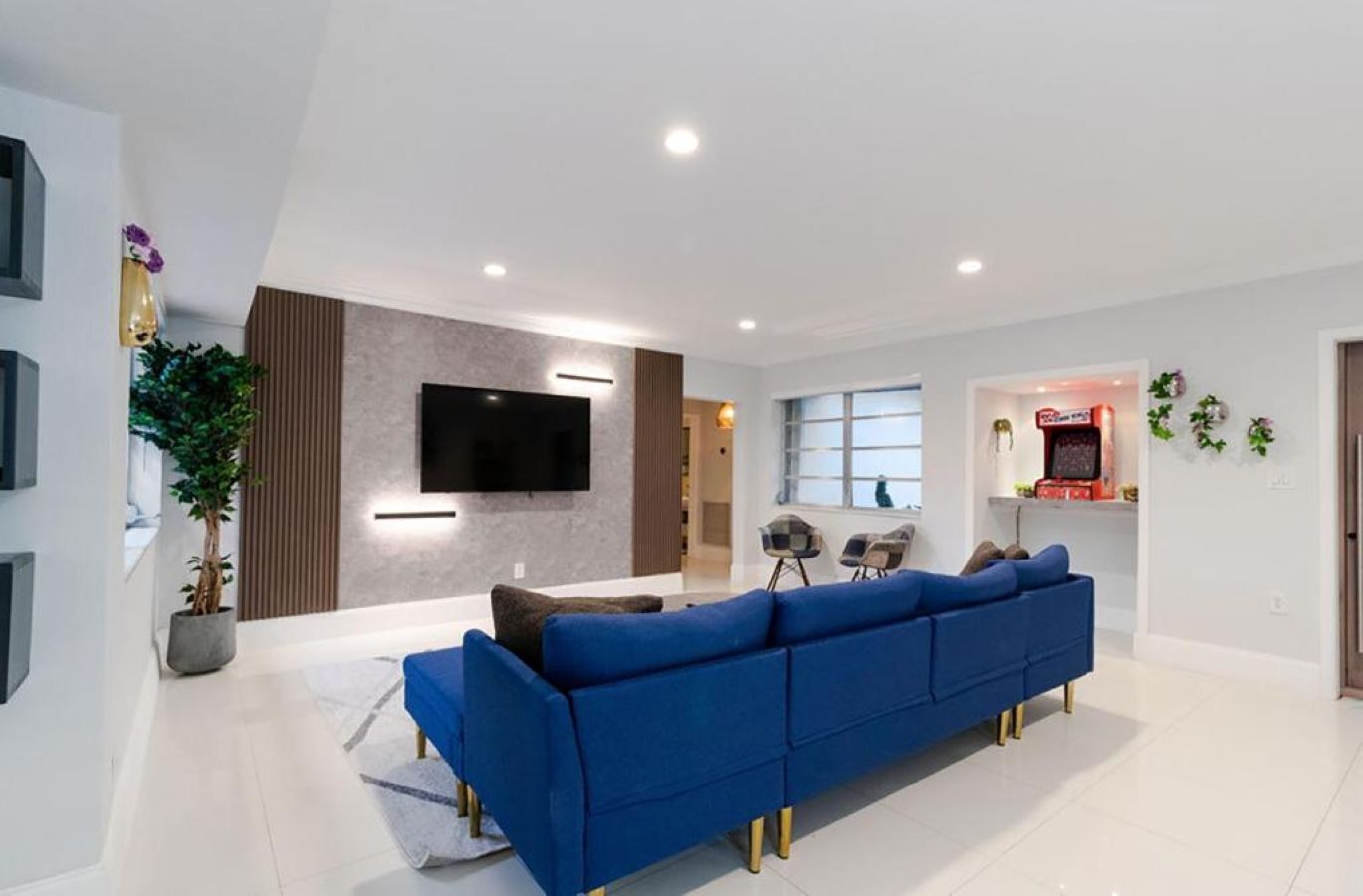 A modern living room with a blue sofa, a flat-screen TV, and a small gaming area.