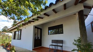 A white building with a tiled porch, a bench, and potted plants. - Cabaña Lewana Campestre (Villa de Leyva)