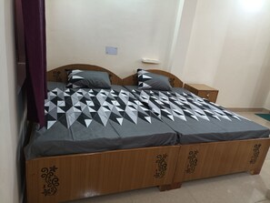 Cama doble con colcha de diseño geométrico, cabecera de madera con adornos tallados, dos mesitas de noche y un pequeño estante fijado a la pared.