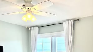 A bedroom with a bed, a ceiling fan, a TV, and a view of the ocean through a window. - Modern Beachfront Condo w/pool Carolina Beach (Carolina Beach)