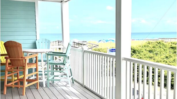A wooden deck with a table and chairs, overlooking a beach. - Modern Beachfront Condo w/pool Carolina Beach (Carolina Beach)