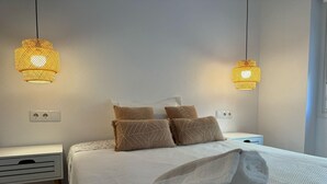 A neatly made bed with a white duvet and multiple pillows, two bedside tables with lamps, and a power outlet on the wall. - Single room for rent for single days or weekends. (Sevilla este)