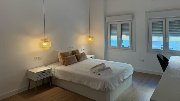A bedroom with a bed, bedside tables, a desk, and a window with blinds. - Single room for rent for single days or weekends. (Sevilla este)