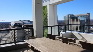 A high-rise balcony with a wooden table and chairs, a vertical garden, and a view of the cityscape including the Omni Hotel.