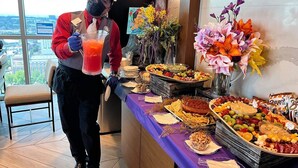 A buffet setup with a variety of food items and a person serving drinks.