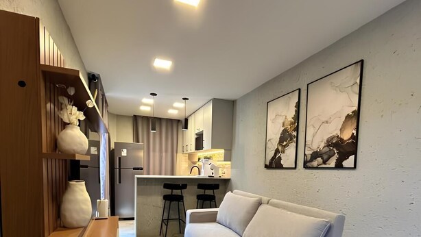 Een moderne woonkamer met een bank, een houten boekenkast en een keuken op de achtergrond.