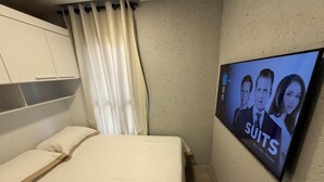 Een hotelkamer met een bed, een televisiescherm waarop een reclame voor 'SUITS' wordt getoond, en een kledingkast.