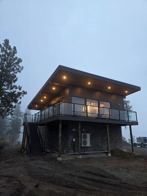 A modern two-story building with a balcony, large windows, and a wooden facade.