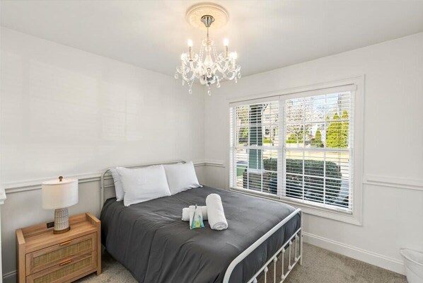 Un dormitorio con cama, una mesita de noche con lámpara, una ventana con persianas y un candelabro.