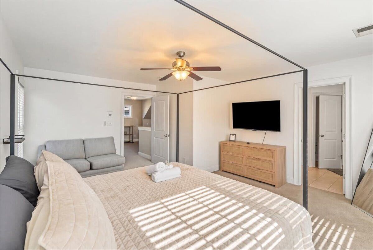Ein Schlafzimmer mit Bett, Sofa, Fernseher, einem Holzschrank und einem Deckenventilator.
