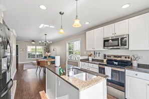 Una cocina moderna con armarios blancos, electrodomésticos de acero inoxidable e iluminación colgante.