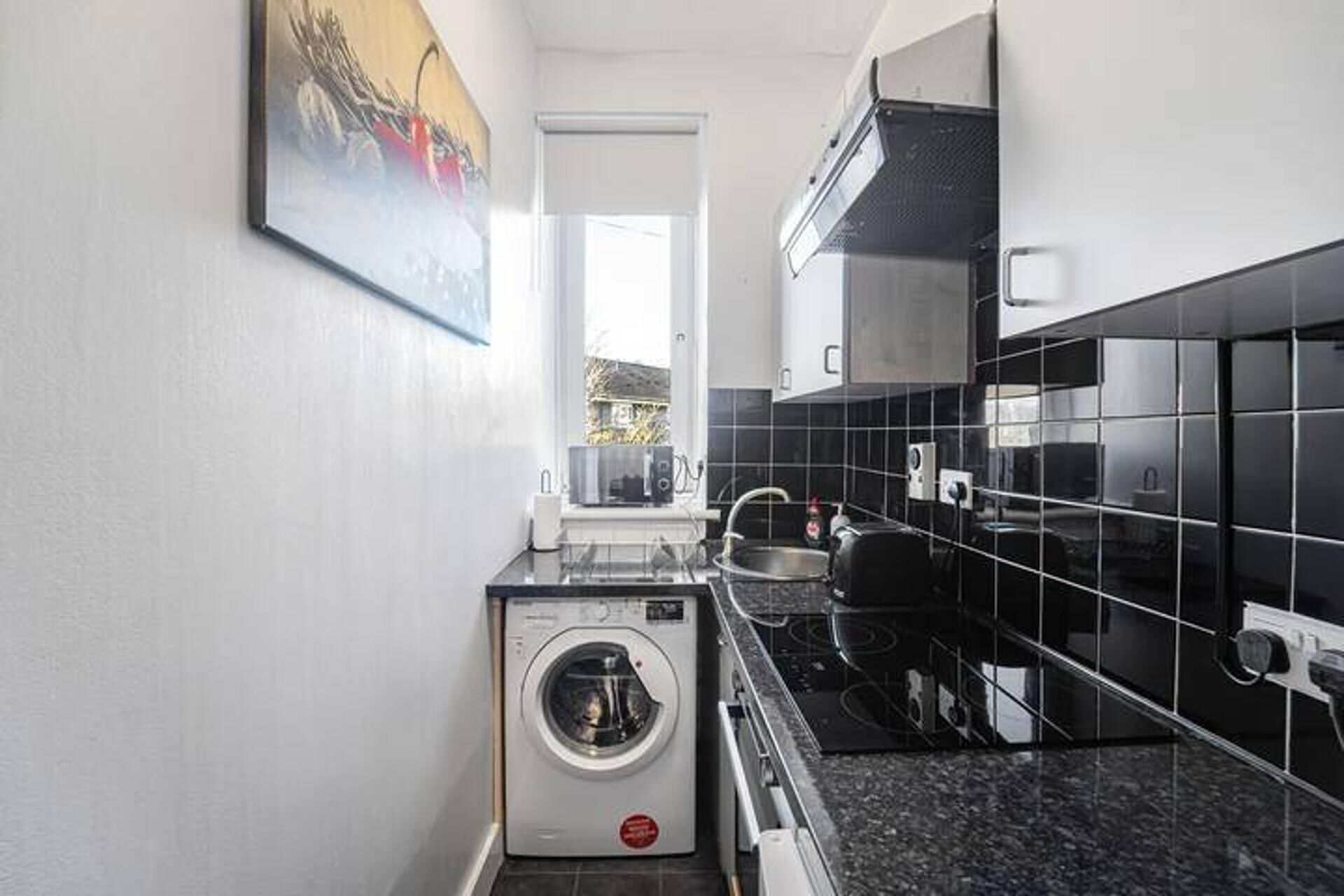 A compact kitchen with a washing machine, a stove, and black tiled walls.