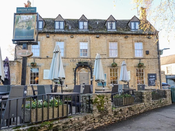 Un bĂątiment traditionnel en pierre, avec une enseigne indiquant « Old Manse Hotel », et des tables Ă lâextĂ©rieur, protĂ©gĂ©es par des parasols.
