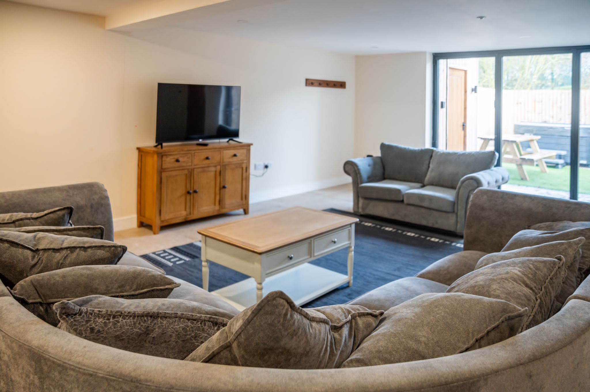 A living room with a sofa, a coffee table, a TV on a wooden cabinet, and a sliding glass door to the outside.