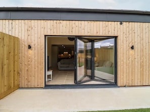 Un bĂątiment moderne avec une façade en bois, une entrĂ©e dotĂ©e dâune porte-fenĂȘtre coulissante et un espace de vie visible, comprenant un canapĂ© et une table Ă manger.