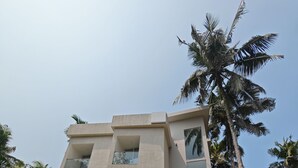 A modern multi-story building with balconies, a garage, and surrounding palm trees. - The Zen Retreat (Kozhikode)