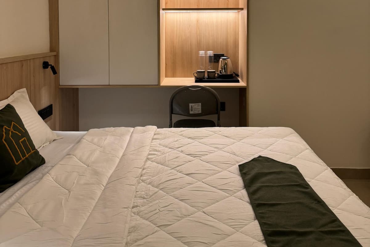 A hotel room with a bed, a desk with a chair, and a wardrobe.