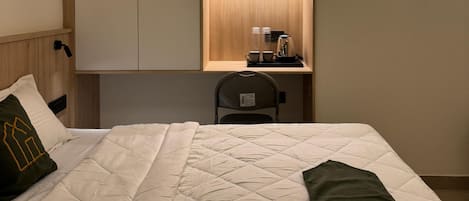 A hotel room with a bed, a desk with a chair, and a wardrobe.