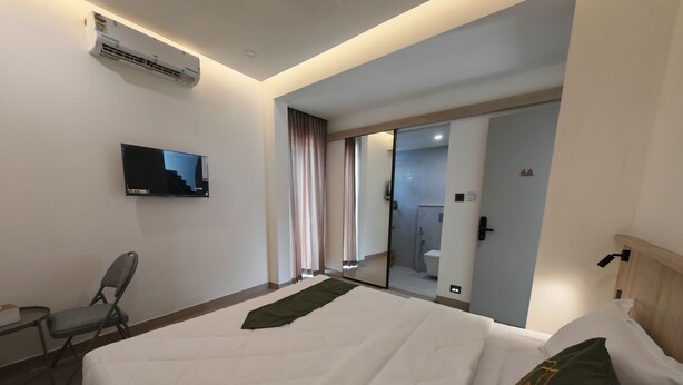 A hotel room with a bed, a chair, a TV, and a bathroom visible through a glass door. - The Zen Retreat (Kozhikode)