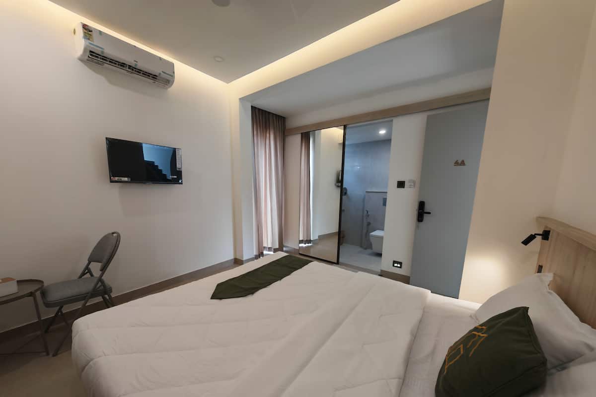 A hotel room with a bed, a chair, a TV, and a bathroom visible through a glass door.