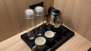 A coffee station with a coffee maker, two mugs, and three glasses on a black tray. - The Zen Retreat (Kozhikode)