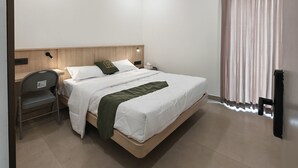 A modern hotel room with a large bed, a desk, a chair, an air conditioning unit, and a window with curtains. - The Zen Retreat (Kozhikode)