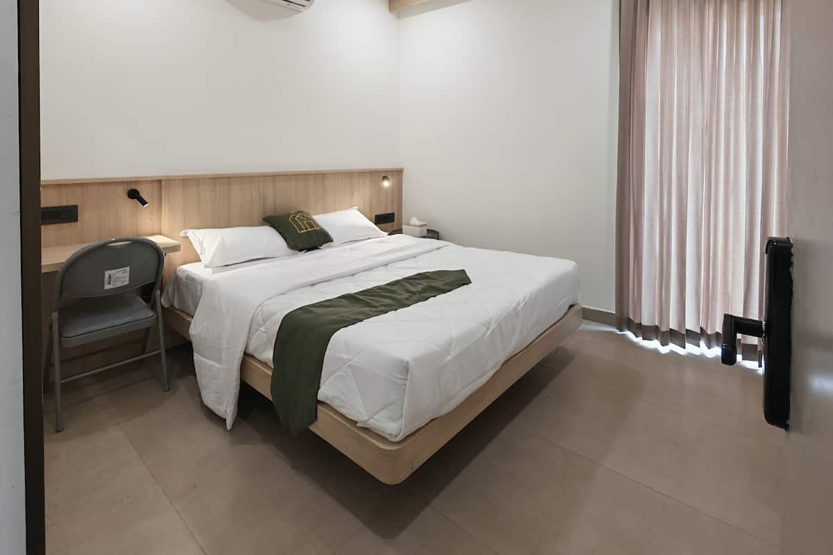 A modern hotel room with a large bed, a desk, a chair, an air conditioning unit, and a window with curtains.