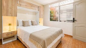 Ein Schlafzimmer mit einem Bett, Nachttischen, einem Fenster mit Jalousien und einer Tür.