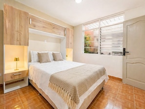 A bedroom with a bed, bedside tables, a window with blinds, and a door. - Private room in a coliving space (Medellín)