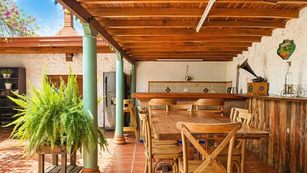Eine Terrasse im Freien mit Holztisch und -stühlen, einem Blumentopf und einer Küchenzeile inklusive Kühlschrank und Fliesenwand.
