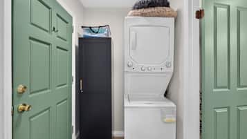 Una sala de lavandería con lavadora y secadora, una puerta con pomo de latón y una bolsa colgada en la pared.