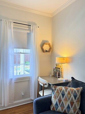A room with a dining table, a chair, a lamp, and a couch with a patterned pillow. - Newly Refreshed | King Bed | Walk to Forsyth (Savannah)