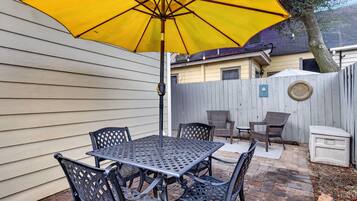 Un patio exterior con una mesa, sillas, un paraguas amarillo y una valla de madera.