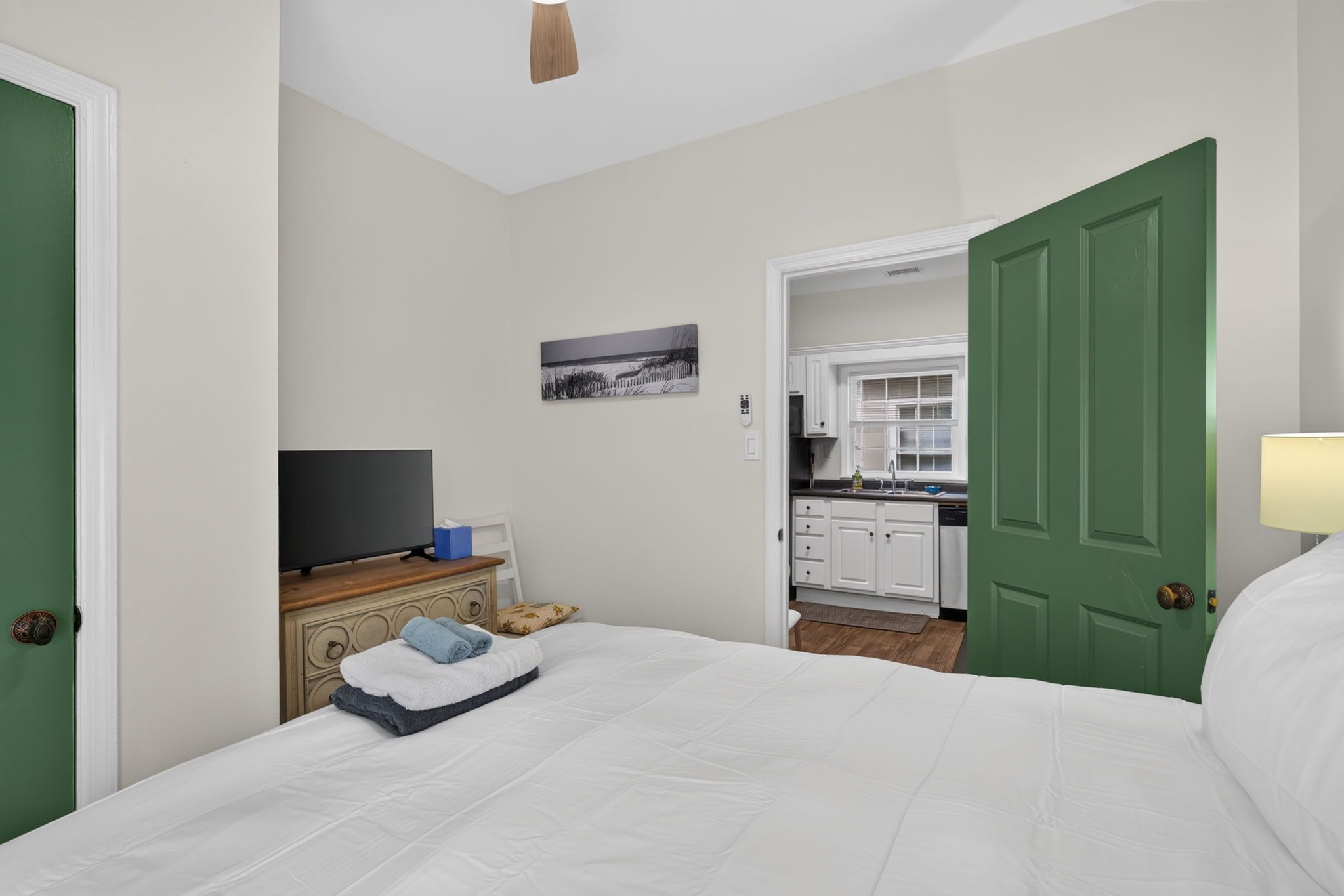 Una camera d'albergo con un letto, una televisione su un comò, un quadro appeso al muro e vista sull'area cucina.