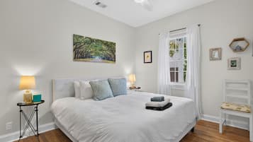 A bedroom with a large bed, a ceiling fan, a window with curtains, and a painting on the wall.