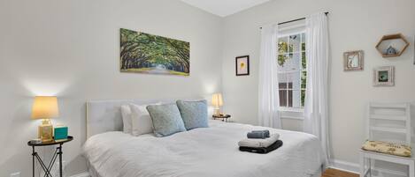 Ein Schlafzimmer mit einem großen Bett, einem Deckenventilator, einem Fenster mit Vorhängen und einem Bild an der Wand.