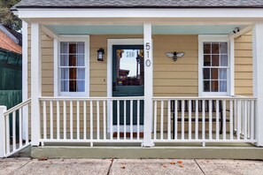 A two-story building with a porch, a front door with a number sign, and a bee decoration. - Historic Cottage | Walk to Forsyth | King + Queen (Savannah)