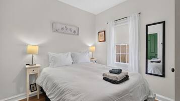 Un dormitorio con una cama grande, mesitas de noche, una ventana con cortinas, un espejo y una pared con un cuadro.