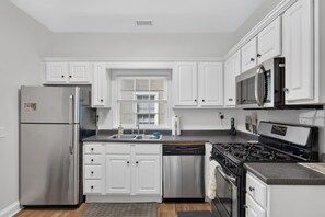 A modern kitchen with white cabinetry, stainless steel appliances, and a granite countertop. - Newly Refreshed | King Bed | Walk to Forsyth (Savannah)