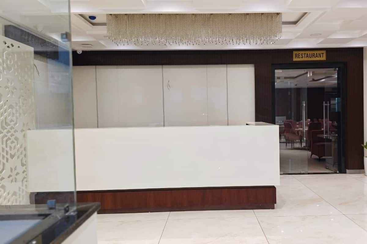 Una moderna zona de recepción con un mostrador blanco, un cartel que dice 'RESTAURANT' sobre la puerta y plantas en macetas.